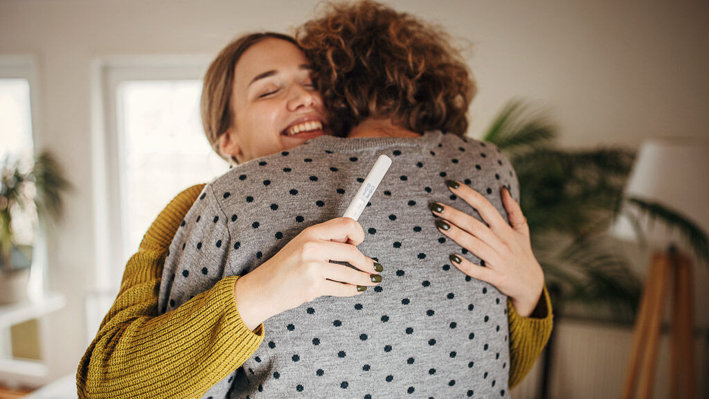 Ein Paar umarmt sich glücklich, sie hält einen Schwangerschaftstest in der Hand.