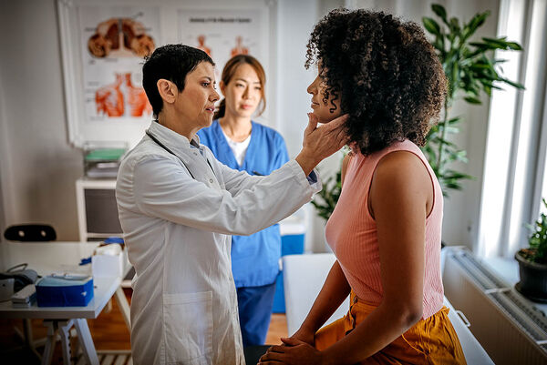 Eine Ärztin untersucht eine Patientin mit einer Tastuntersuchung an ihrem Hals.