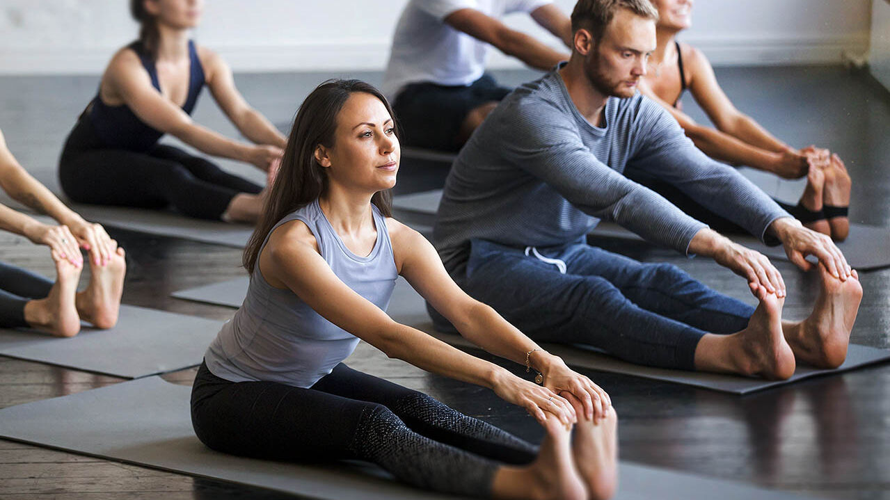 Eine Frau macht in einer Gruppe einen Yoga-Kurs und dehnt sich.