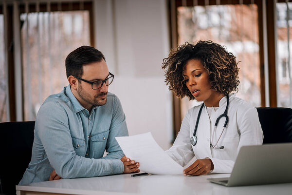 Eine Ärztin und ihr Patient sitzen an einem Tisch und sie erklärt ihm anhand eines Dokuments verschiedene Behandlungsmöglichkeiten.