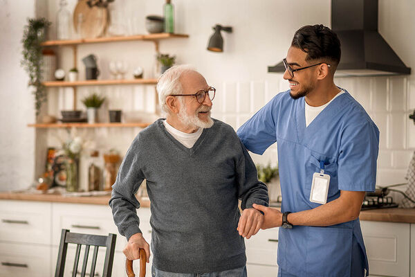 Ein älterer Mann wird von einem Pfleger beim Laufen gestützt.