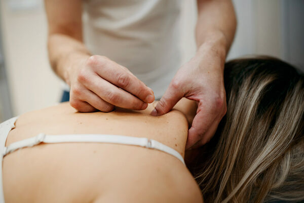 Einer Frau wird eine Akupunktur-Nadel im Nacken angebracht.