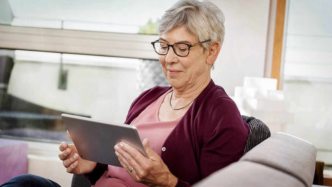 Eine ältere Frau sitzt auf dem Sofa und benutzt ihr Tablet.