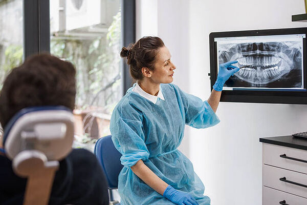 Eine Zahnärztin erklärt einem Patienten das Röntgenbild seines Kiefers.