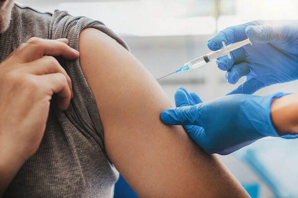 Eine medizinische Fachkraft spritzt eine Impfung in den Oberarm eines Patienten.