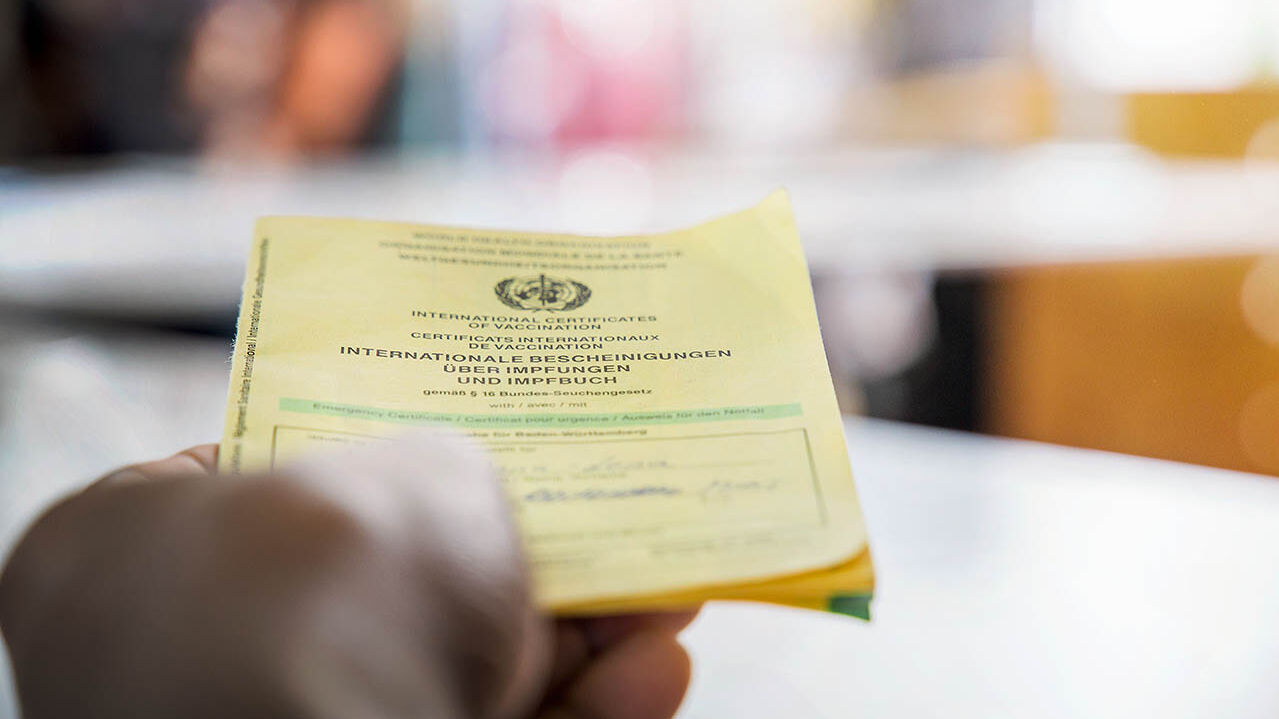 Eine Hand hält den gelben Impfpass.