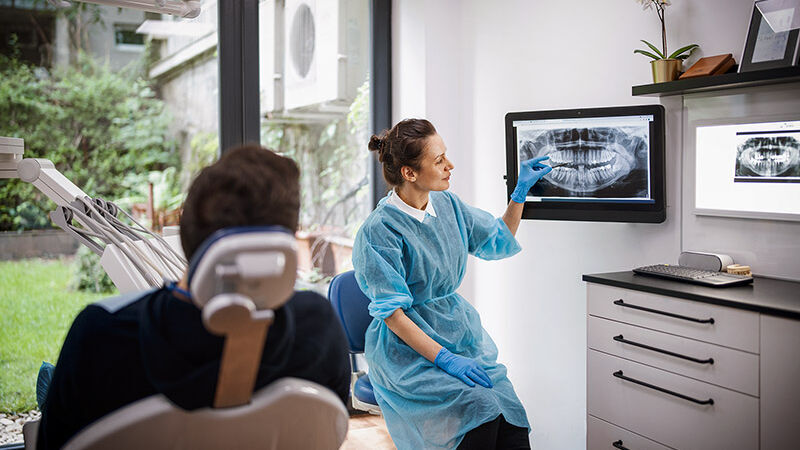 Eine Zahnärztin erklärt einem Patienten das Röntgenbild seines Kiefers.