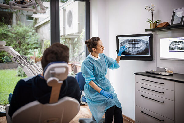 Eine Zahnärztin erklärt einem Patienten das Röntgenbild seines Kiefers.