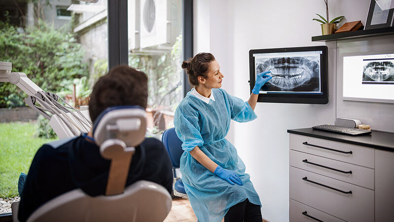 Eine Zahnärztin erklärt einem Patienten das Röntgenbild seines Kiefers.
