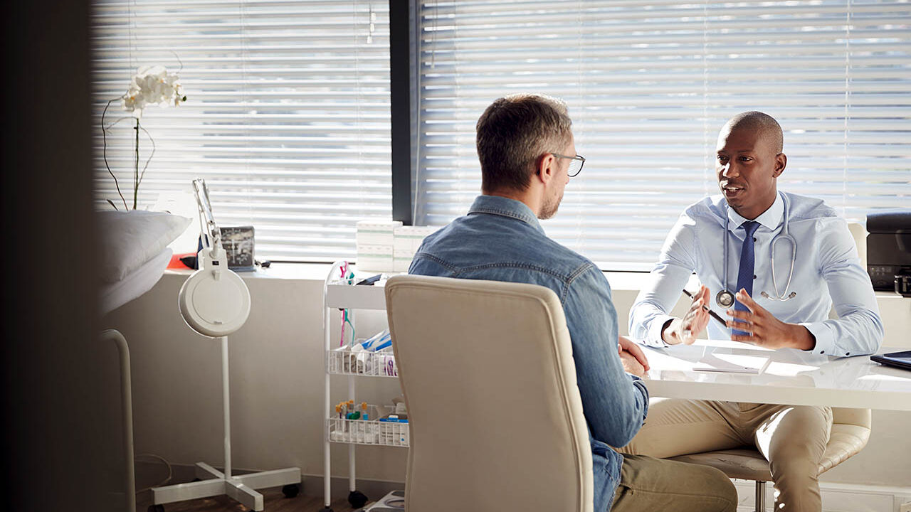 Ein Patient sitzt in einem Behandlungsraum seinem Arzt gegenüber und sie besprechen sich.