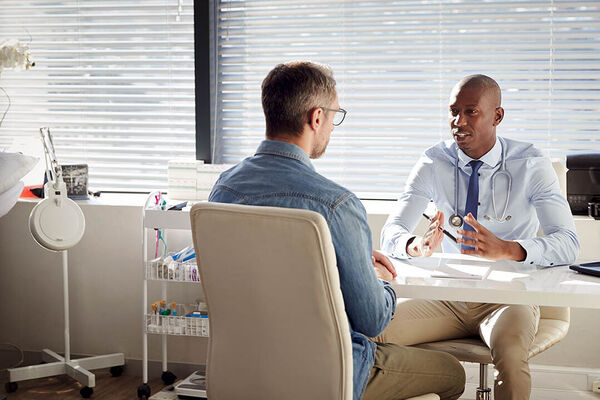 Ein Patient sitzt in einem Behandlungsraum seinem Arzt gegenüber und sie besprechen sich.