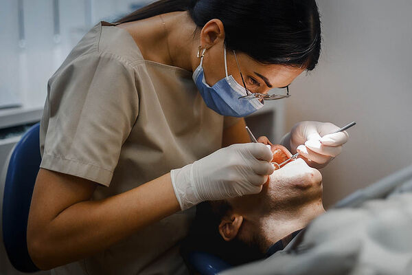 Eine Zahnarzthelferin kontrolliert die Zähne eines Patienten, der auf der Behandlungsliege liegt.