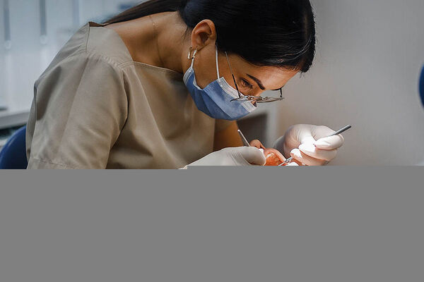 Eine Zahnarzthelferin kontrolliert die Zähne eines Patienten, der auf der Behandlungsliege liegt.