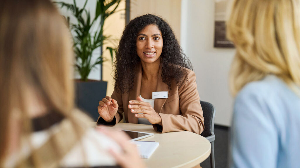 Eine Mitarbeiterin der SBK sitzt mit einer Kundin und ihrer Tochter an einem Tisch und berät sie.