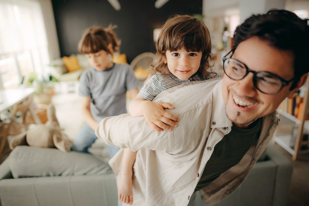Ein Mann spielt mit seinen Kindern im Wohnzimmer.