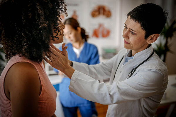 Eine Ärztin untersucht eine junge Frau an ihrem Hals mittels einer Tastuntersuchung.