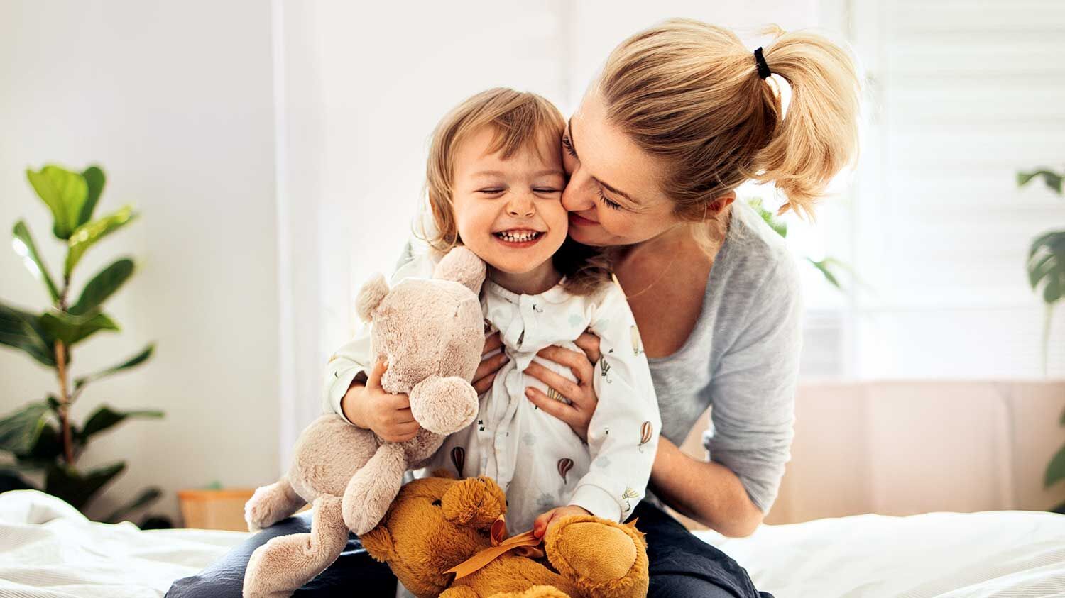 Eine blonde Frau sitzt mit ihrem Kind auf dem Bett