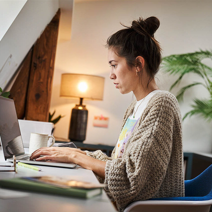 Eine Frau sitzt in ihrem Homeoffice und arbeitet an ihrem Laptop.