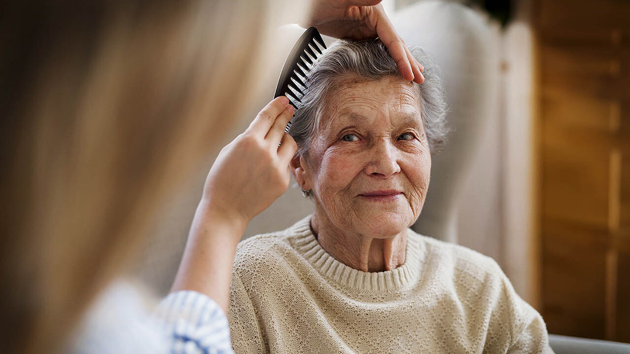 Einer älteren Frau werden ihre Haare von ihrer Enkelin gekämmt.