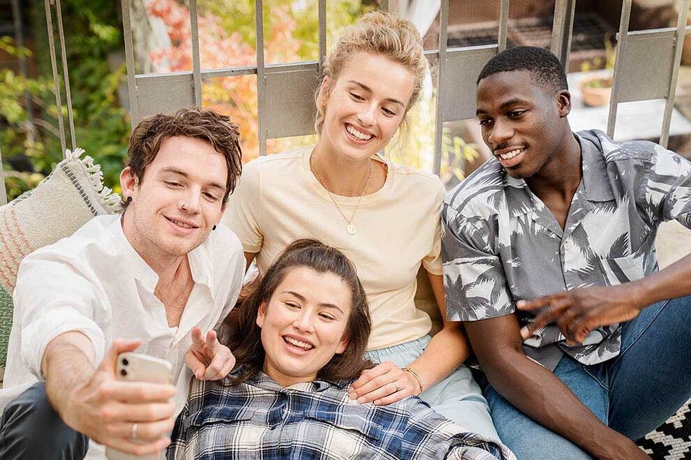 Eine Gruppe junger Erwachsener sitzt zusammen auf einem Balkon und macht ein Selfie zusammen.