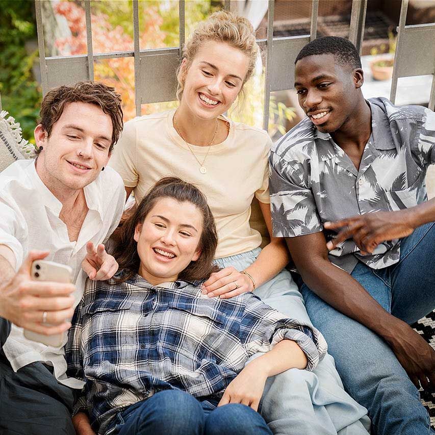 Eine Gruppe junger Erwachsener sitzt zusammen auf einem Balkon und macht ein Selfie zusammen.