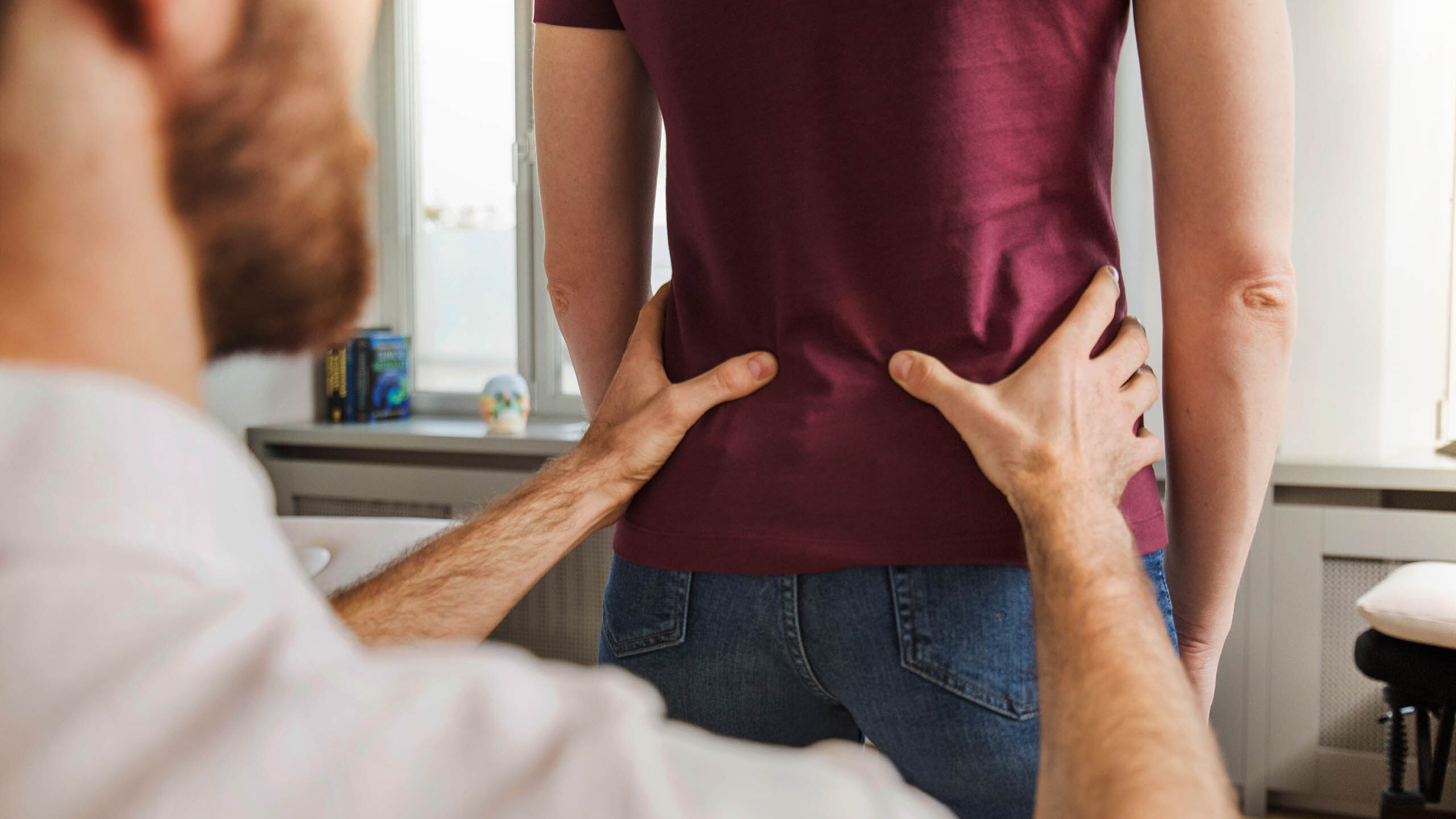 Ein Osteopath untersucht den unteren Rücken einer Patientin.