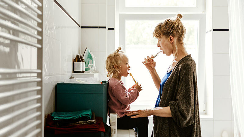 Eine Frau ist mit ihrer kleinen Tochter im Bad und sie putzen sich gemeinsam die Zähne.