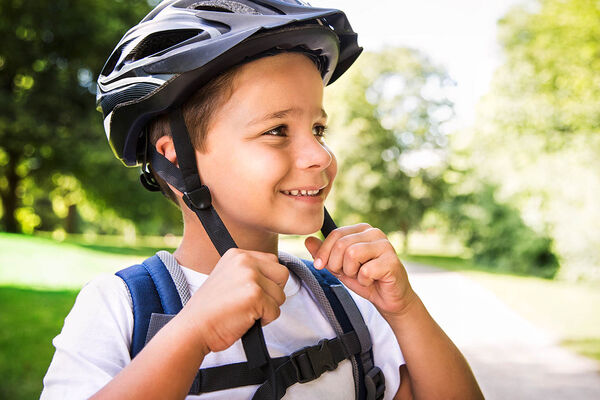 Ein Junge setzt gerade seinen Fahrradhelm auf und freut sich auf die Tour.