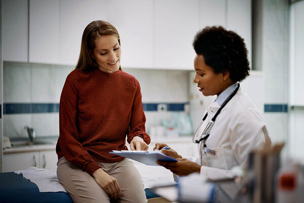 Eine Patientin sitzt auf einer Liege im Behandlungsraum und bespricht mit einer Ärztin ihre Behandlungsergebnisse.