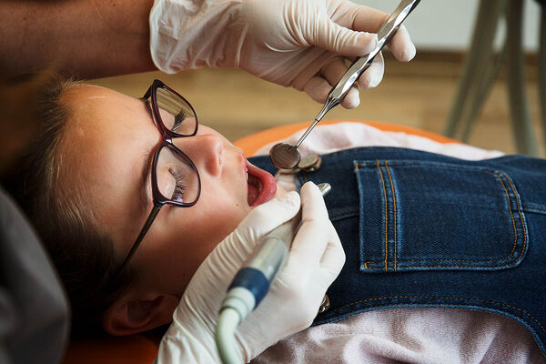 Eine Zahnärztin untersucht die Zähne eines jungen Mädchens, welches auf der Behandlungsliege liegt.