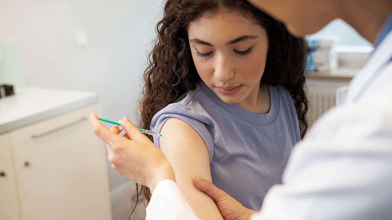 Ein Teenager bekommt von einer Ärztin eine Impfung in den Oberarm.
