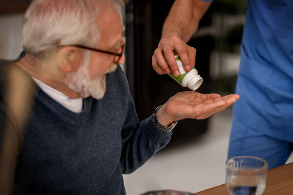 Eine Pflegekraft hilft einem älteren Mann bei der Einnahme von Medikamenten.