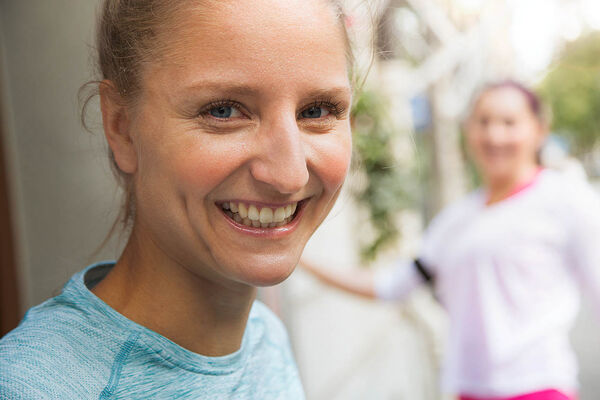 Eine junge Frau lacht während dem Sport mit einer Freundin glücklich in die Kamera. 