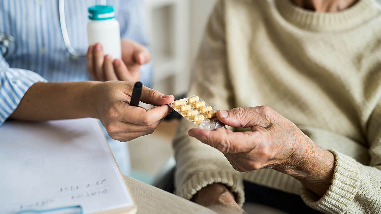 Eine Ärztin gibt einer älteren Frau bei einem Hausbesuch Medikamente.