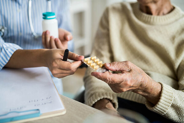 Eine Ärztin gibt einer älteren Frau bei einem Hausbesuch Medikamente. 