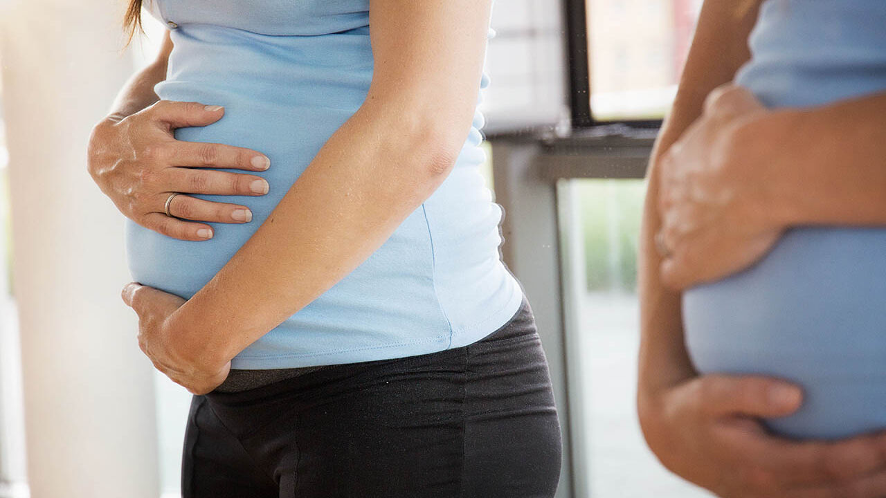 Eine schwangere Frau berührt ihren Bauch und betrachtet sich im Spiegel.