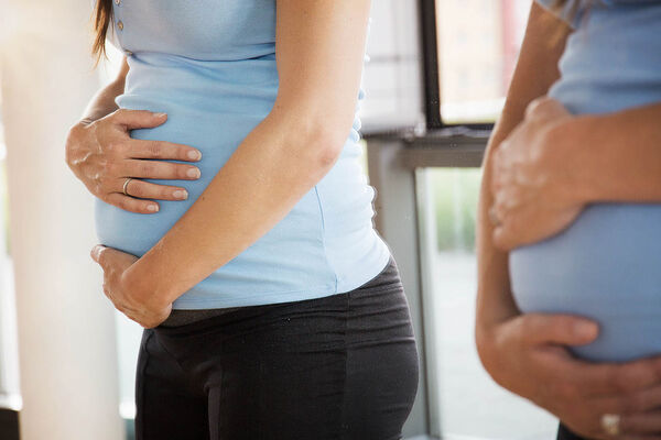 Eine schwangere Frau berührt ihren Bauch und betrachtet sich im Spiegel.