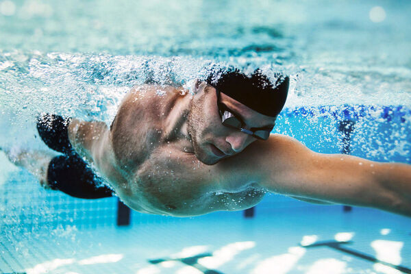 Ein Mann wird beim Schwimmen unter Wasser gezeigt. Er trägt eine Taucherbrille und eine Badekappe.