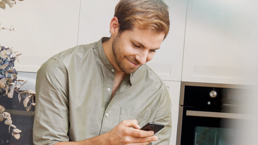 Ein junger Mann benutzt sein Mobiltelefon und lächelt.