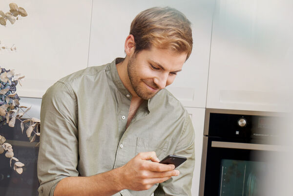 Ein junger Mann benutzt sein Mobiltelefon und lächelt.