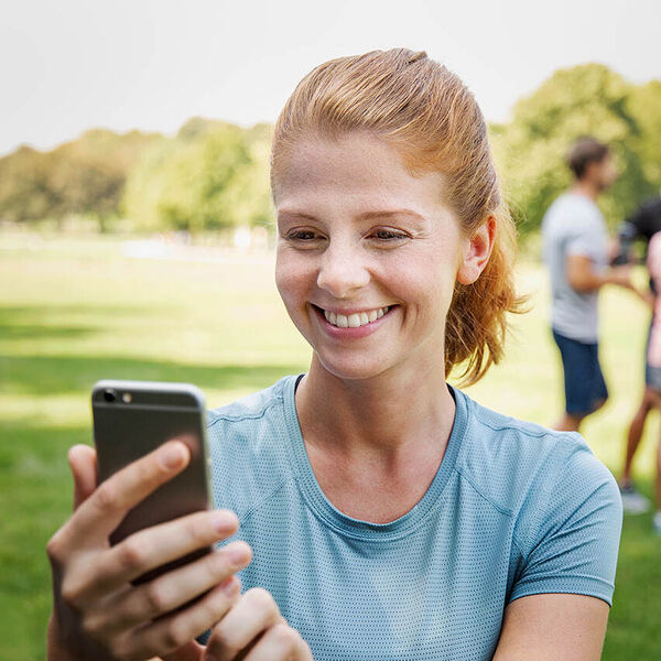 Eine Frau ist mit Freunden im Park und macht mit ihrem Handy einen Videoanruf. 