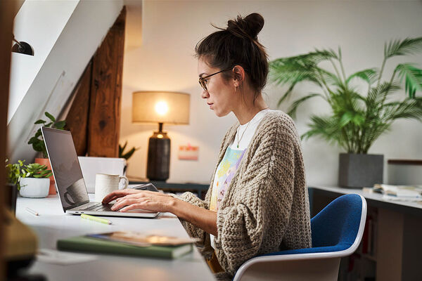 Eine Frau sitzt in ihrem Homeoffice und arbeitet an ihrem Laptop.