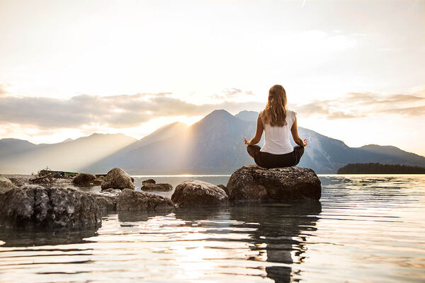 Eine junge Frau sitzt auf einem Stein an einem See und meditiert.