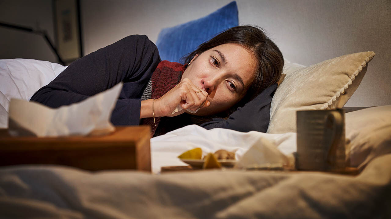 Eine Frau liegt mit einer Erkältung krank im Bett.