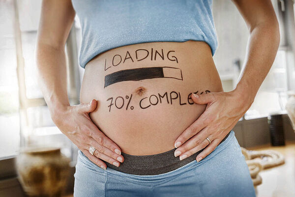 Eine schwangere Frau hält ihren Bauch, auf dem die Aufschrift "Loading 70%" steht.