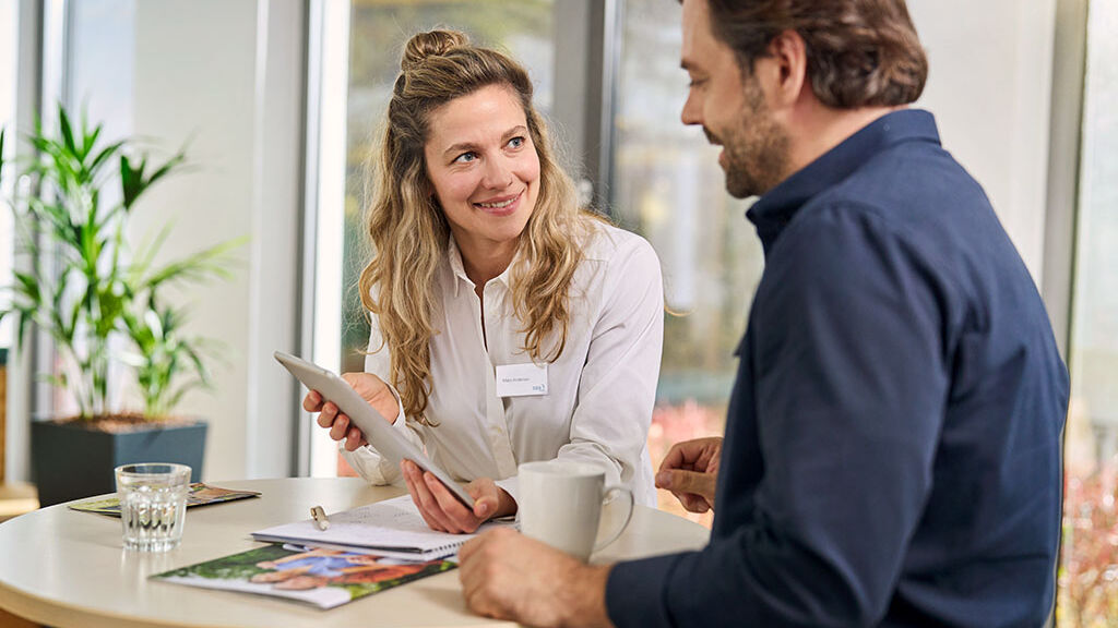 Eine Mitarbeiterin der SBK berät einen Versicherten und zeigt ihm etwas auf einem Tablet.