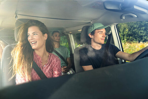 Eine Gruppe junger Erwachsener sitzt mit offenen Fenstern im Auto und fährt gemeinsam weg.