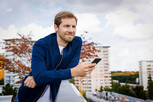 Ein Mann steht an einem Geländer angelehnt und benutzt sein Handy.