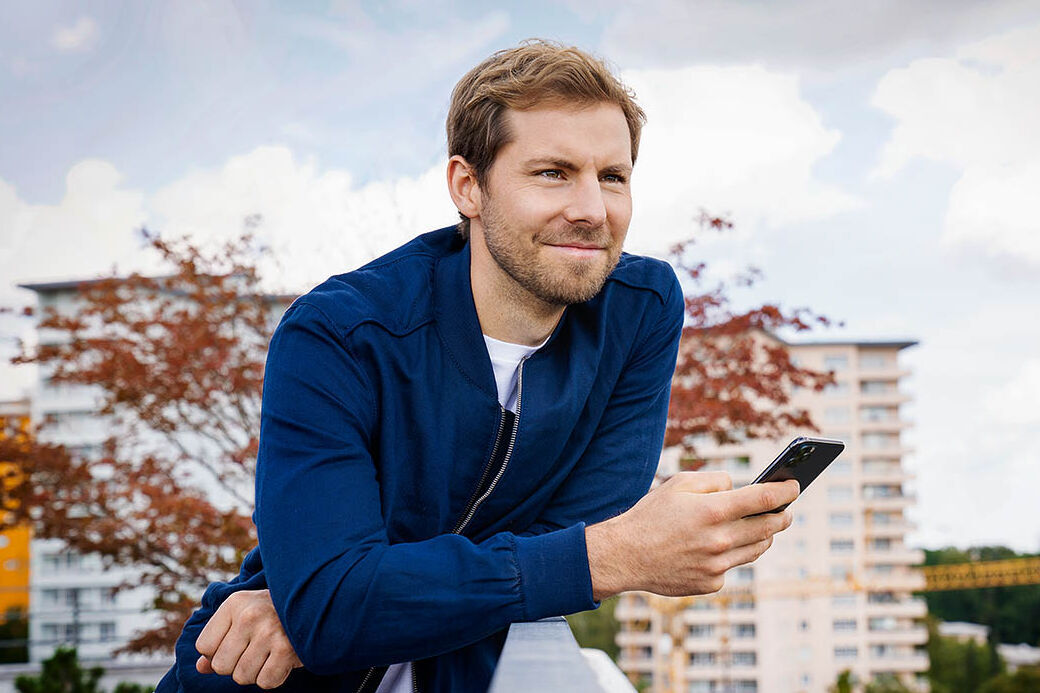Ein Mann steht an einem Geländer angelehnt und benutzt sein Handy.