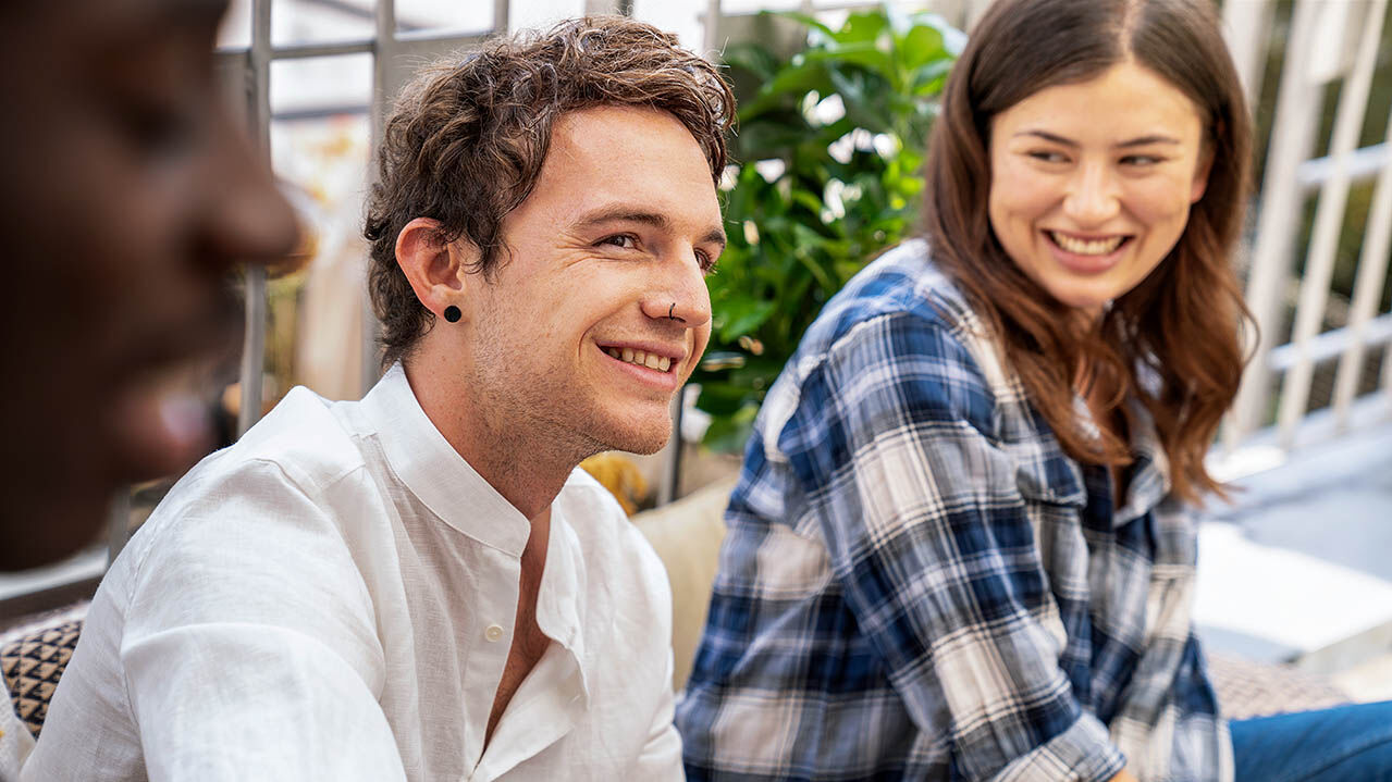 Zwei junge Erwachsene sitzen zusammen auf einer Terrasse und lachen gemeinsam.